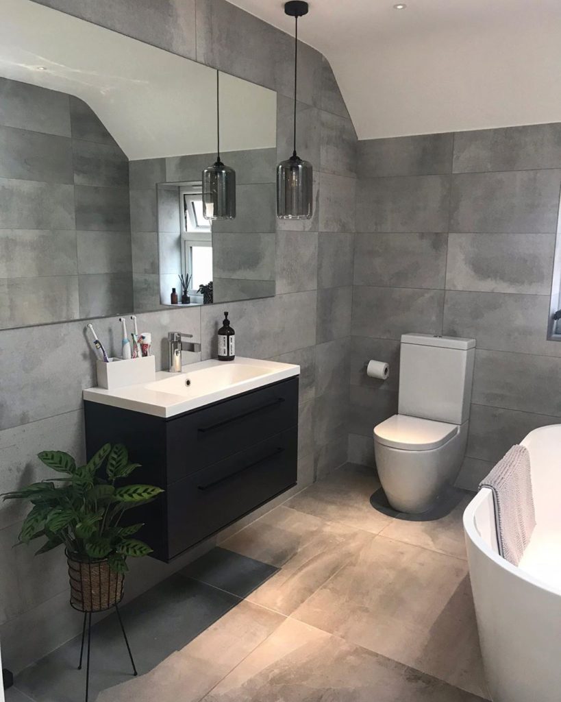 bathroom with gray stone tile on walls hanging pendant light and modern bathtub and toilet