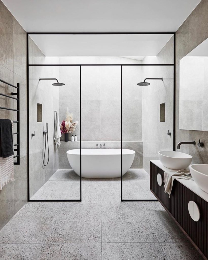 gray bathroom with natural stone floors and double shower heads with matte black fixtures