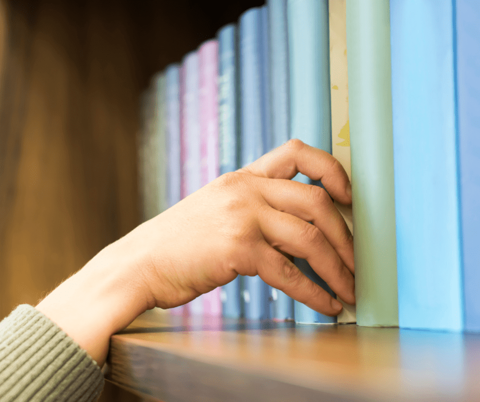 A person's hand pulling a book from a shelf