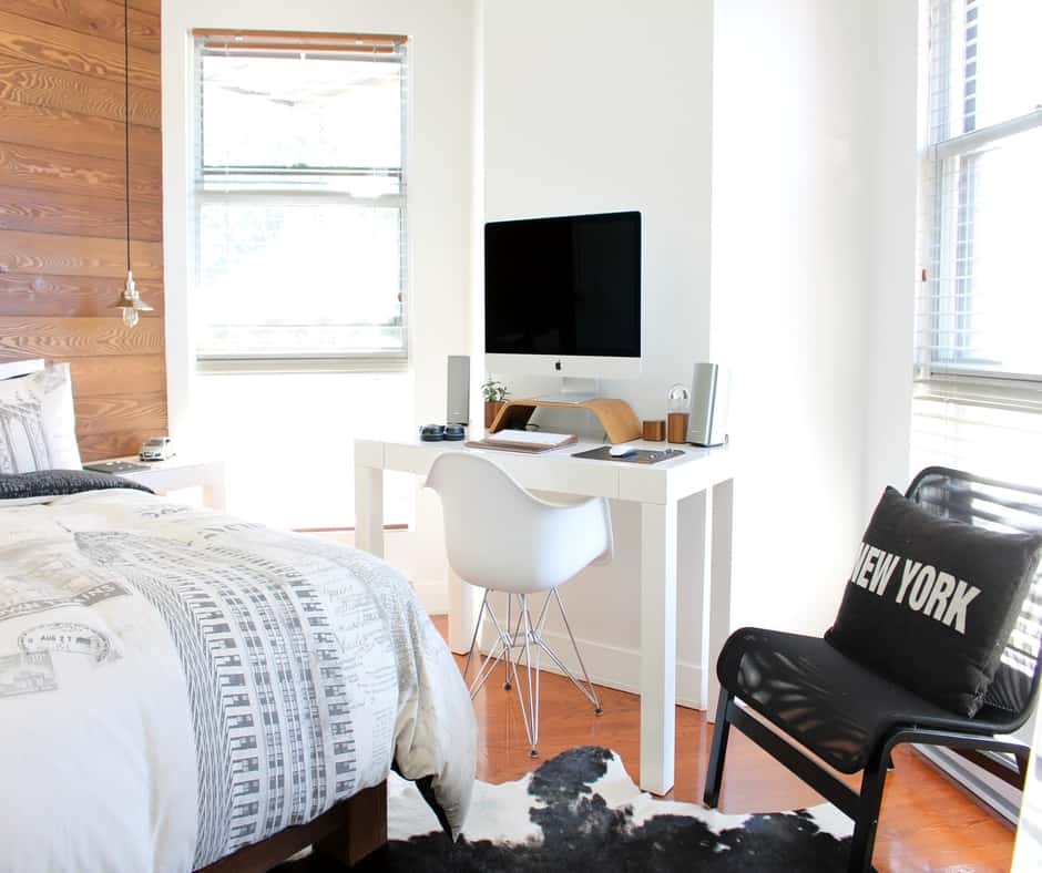 Simple small bedroom that is well lit, with bed, and desk area 