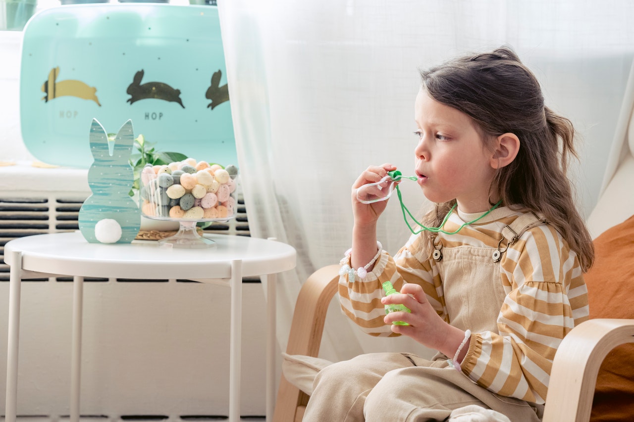 A girl blowing bubbles beside a table with a radiator behind it