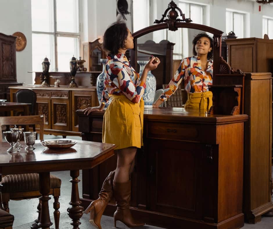 A room with dressers. One dresser with a mirror and a lady looking at herself through the mirror