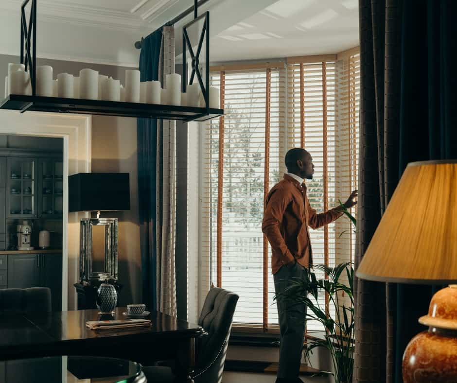 Living area with a man looking through the window with wooden blinds