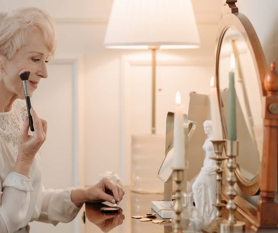 Woman doing her make up looking through a round mirror on top of dresser