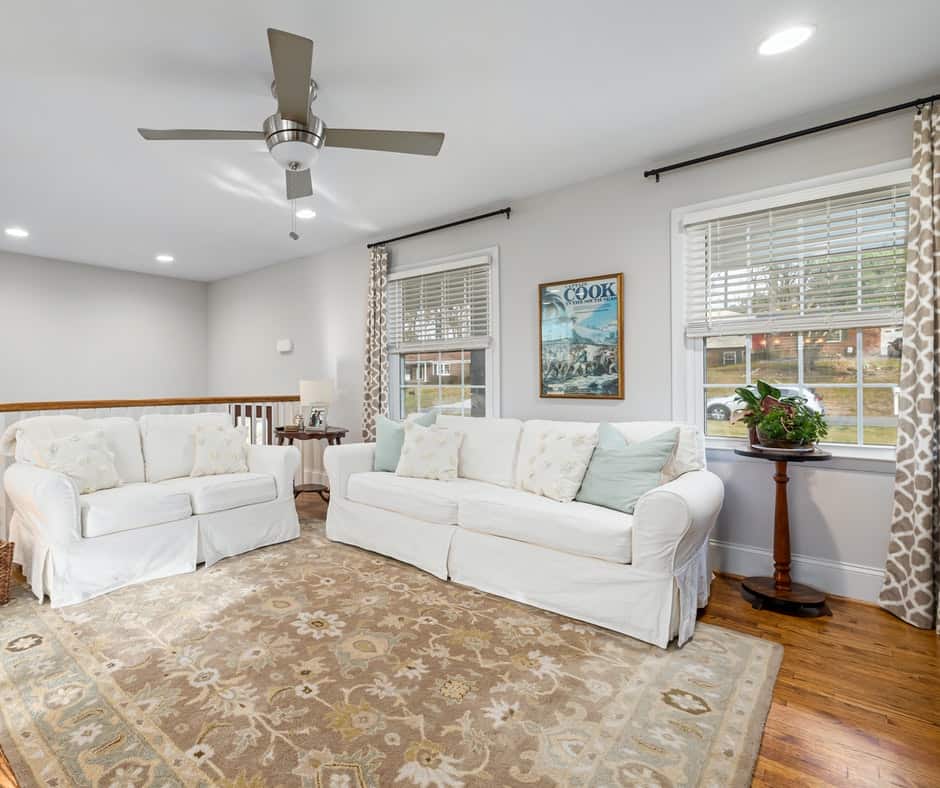 Sitting area next to stairway with a carpet, sofa and window with blinds