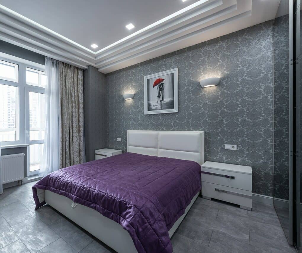 Purple colored bed sheet on white bed frame in a gray-walled bedroom