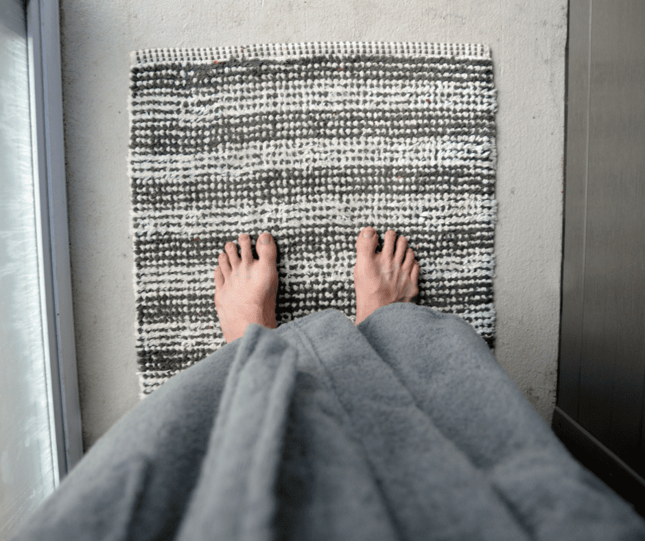 Focuses shot of a person's feet on bathroom rug