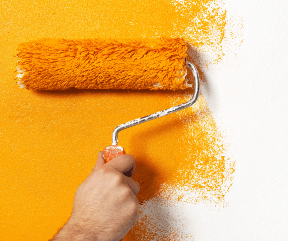 Man holding painting a wall with mustard-colored paint