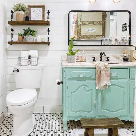 colorful farmhouse bathroom with teal vanity and yellow sconces